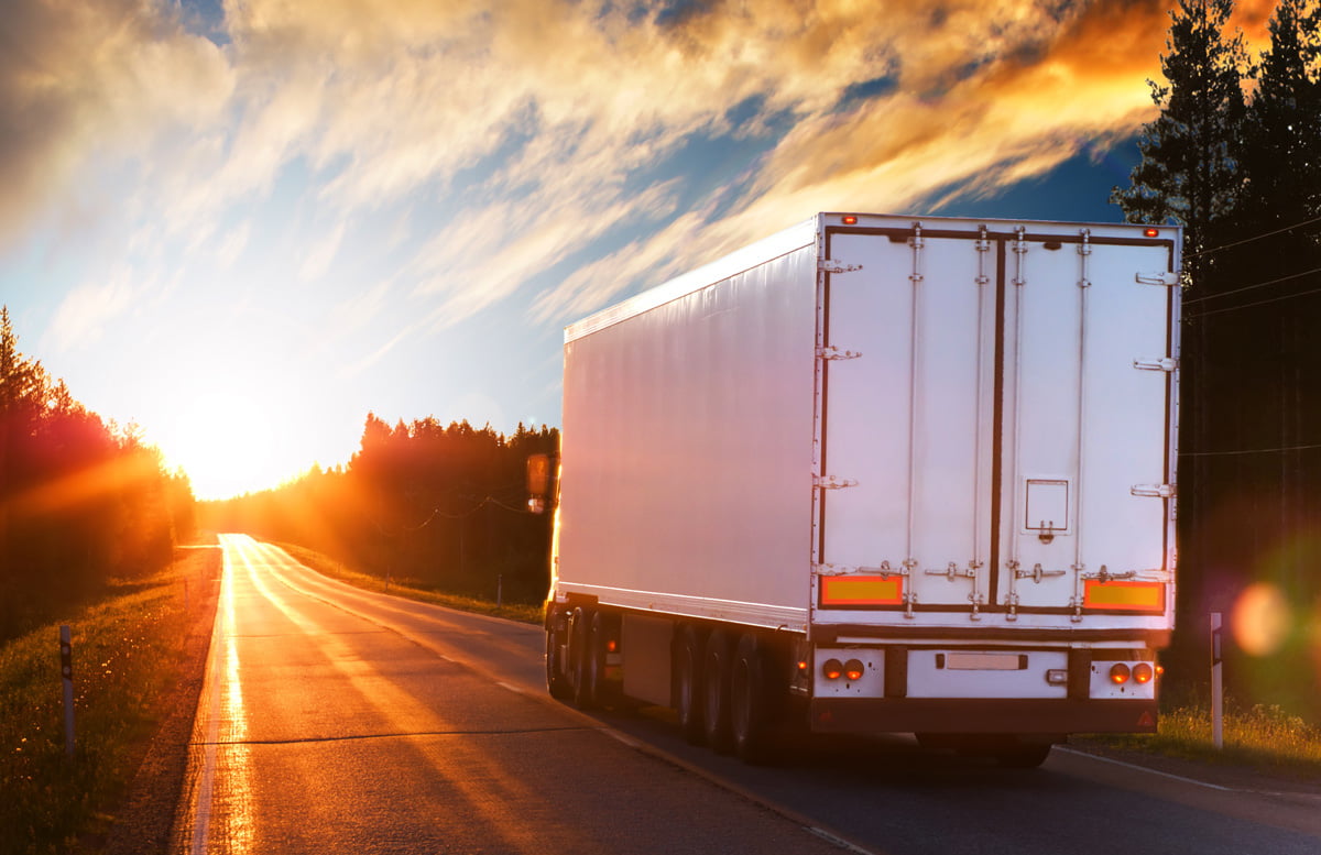 A white semi truck driving toward a sunset in El Paso.