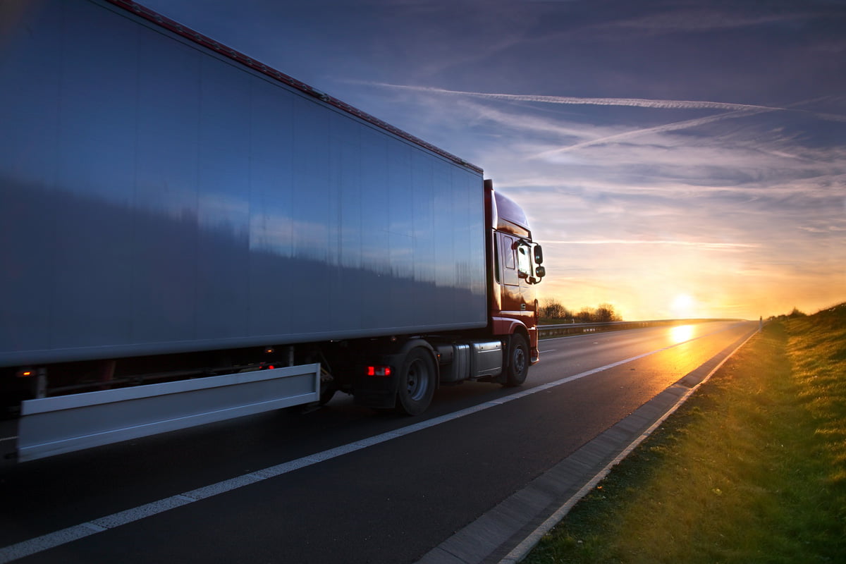 A white and red semi-truck driving towards sunset in El Paso.