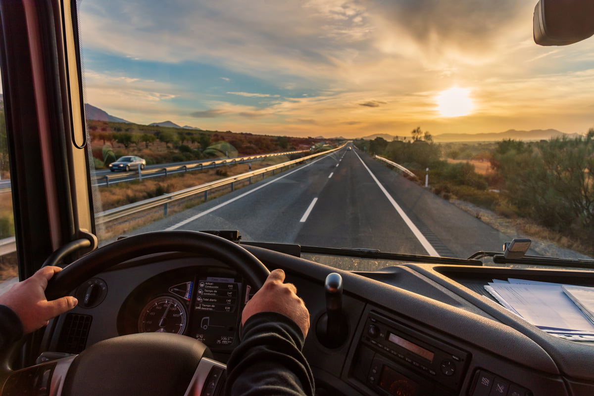 The view out of the windshield of a truck that shows the highway and a person’s hands on the steering wheel.