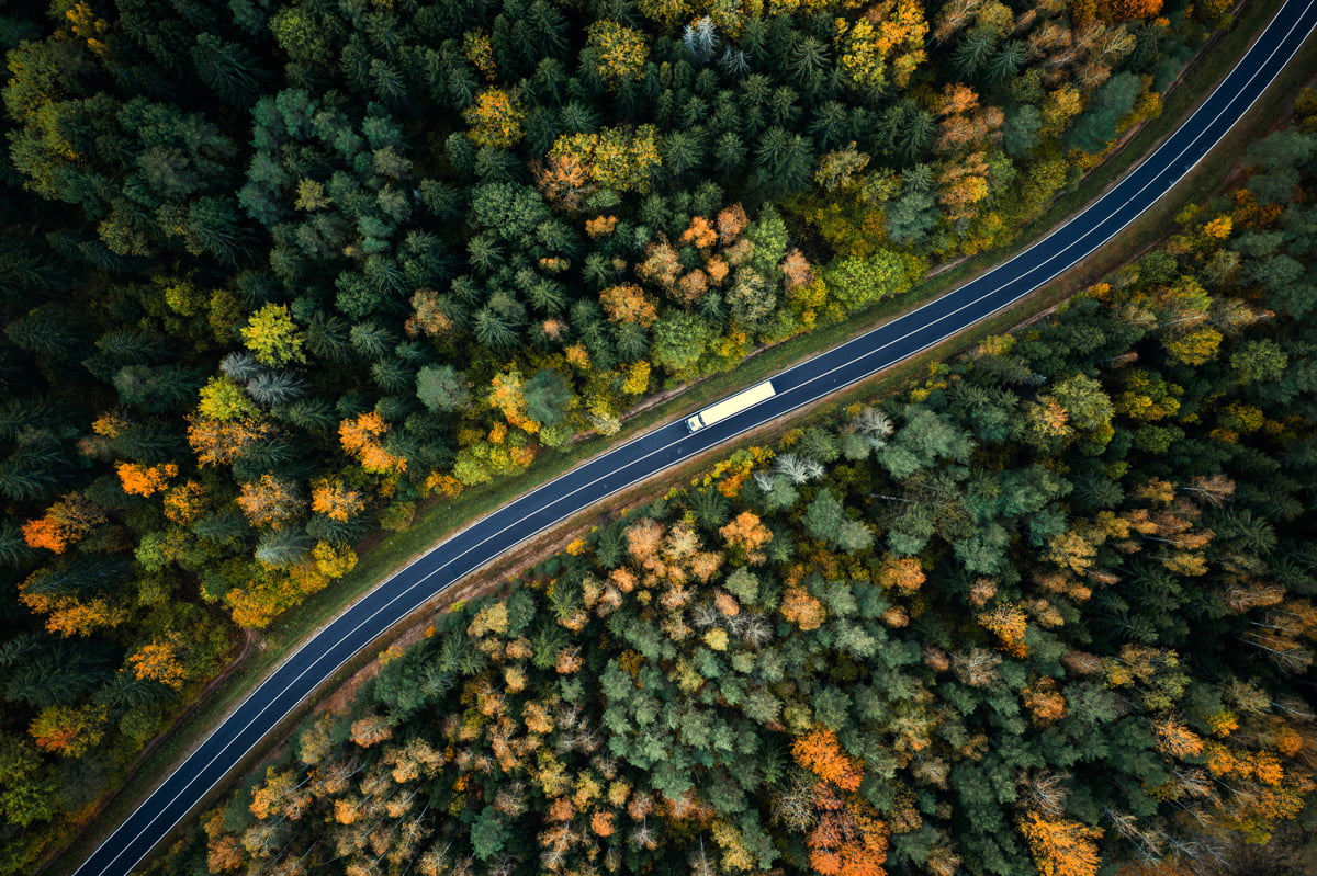 An aerial view of a white truck driving on a highway through the forest in El Paso.